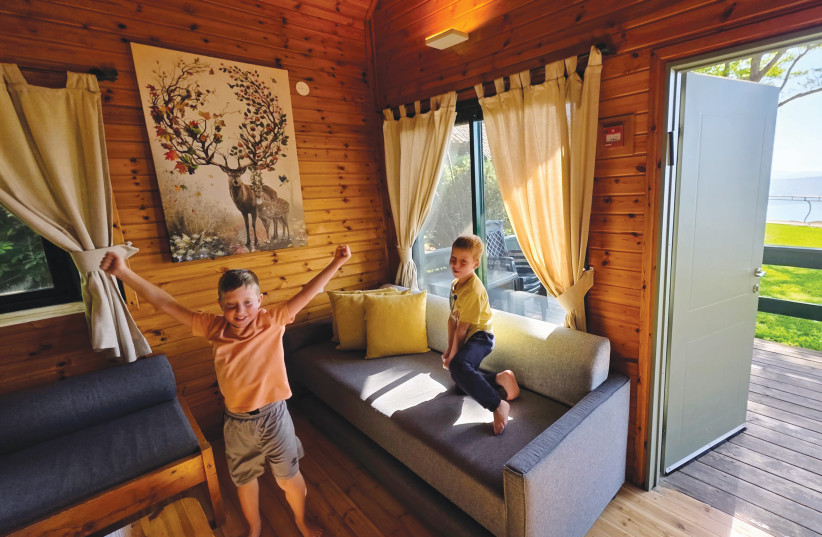 Inside the family cabin: The inviting timber interior reveals a thoughtful multi-level design featuring an attic loft for children, while the open doorway frames a direct view of green lawns and the shimmering lake outside. (credit: NOAM BEDEIN)