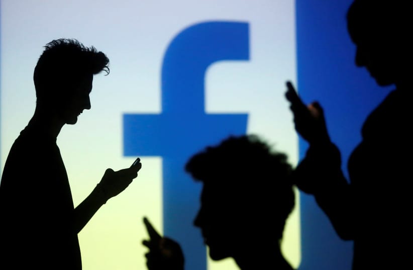 People are silhouetted as they pose with mobile devices in front of a screen projected with a Facebook logo, in this picture illustration taken in Zenica October 29, 2014.  (credit: REUTERS/DADO RUVIC)