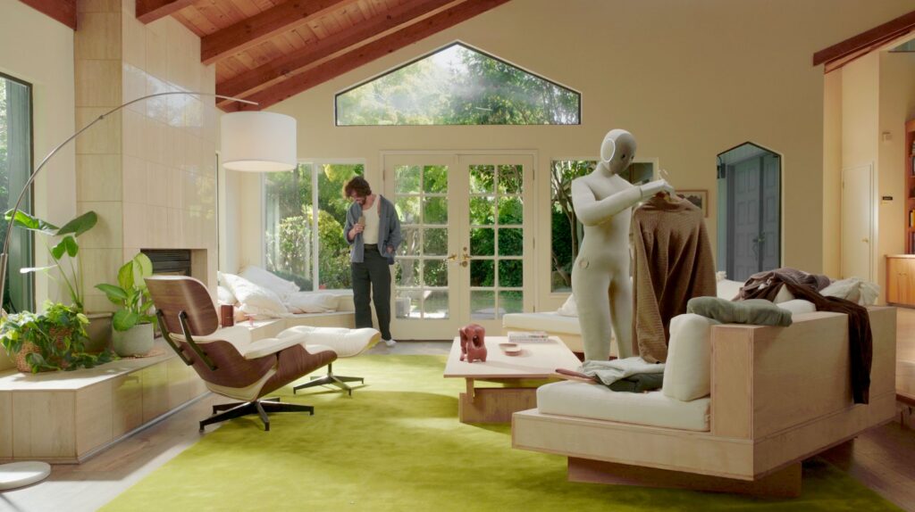 NEO home robot holding a sweater in a living room, in a 1X product photograph.