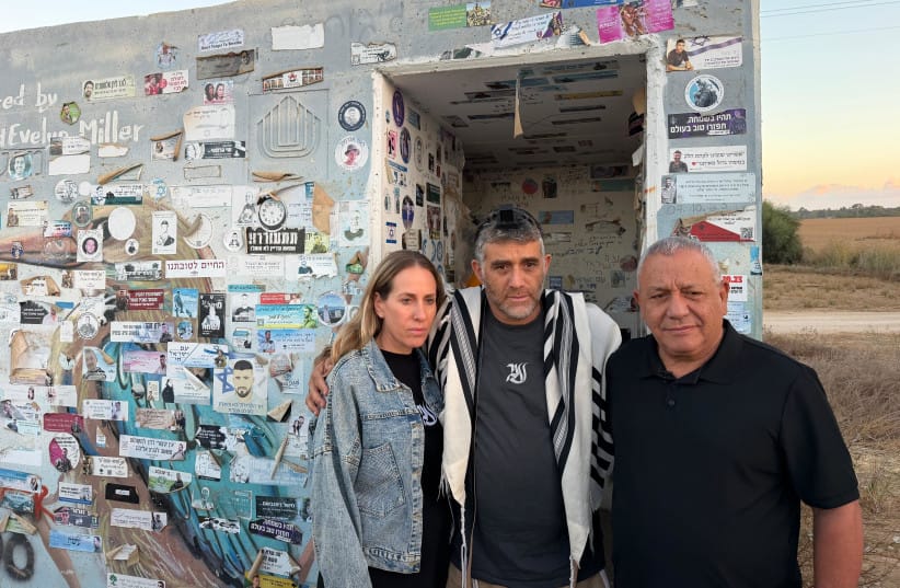Yashar party chairman Gadi Eisenkot stands with the parents of Aner Shapira in front of the bomb shelter where he was killed three years earlier, on October 7, 2026.  (credit: Courtesy)