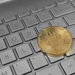 A physical bitcoin token resting on a laptop keyboard.