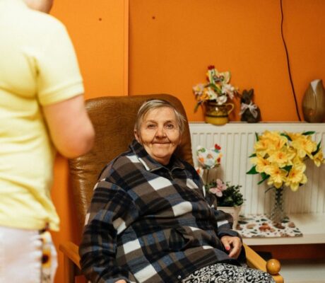 An older resident in an armchair with a caregiver nearby. Illustrative archive, not a CMS enforcement subject.