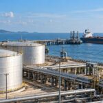 Fuel storage tanks and pipelines beside a tanker and Indian flag.