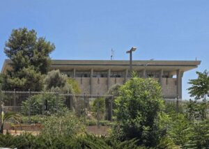 Archive photo: the Knesset building behind greenery and a fence in Jerusalem, July 16, 2025. Not the 2026 count.