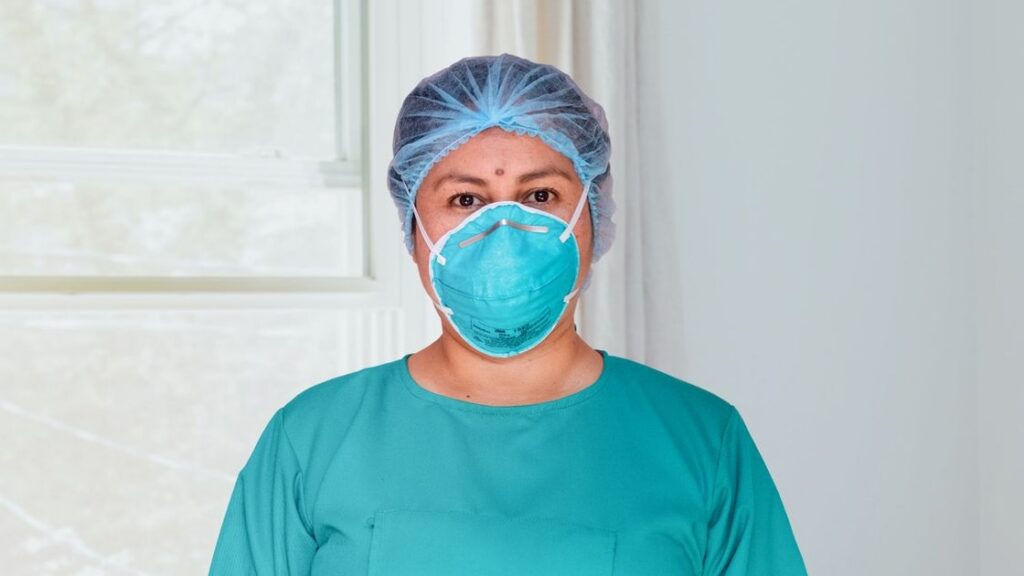 A masked healthcare professional in an illustrative clinical-setting archive photo. Not an individual return-to-work decision.