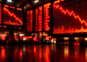 Blurred red stock market screens showing falling charts glowing in a dark trading hall.