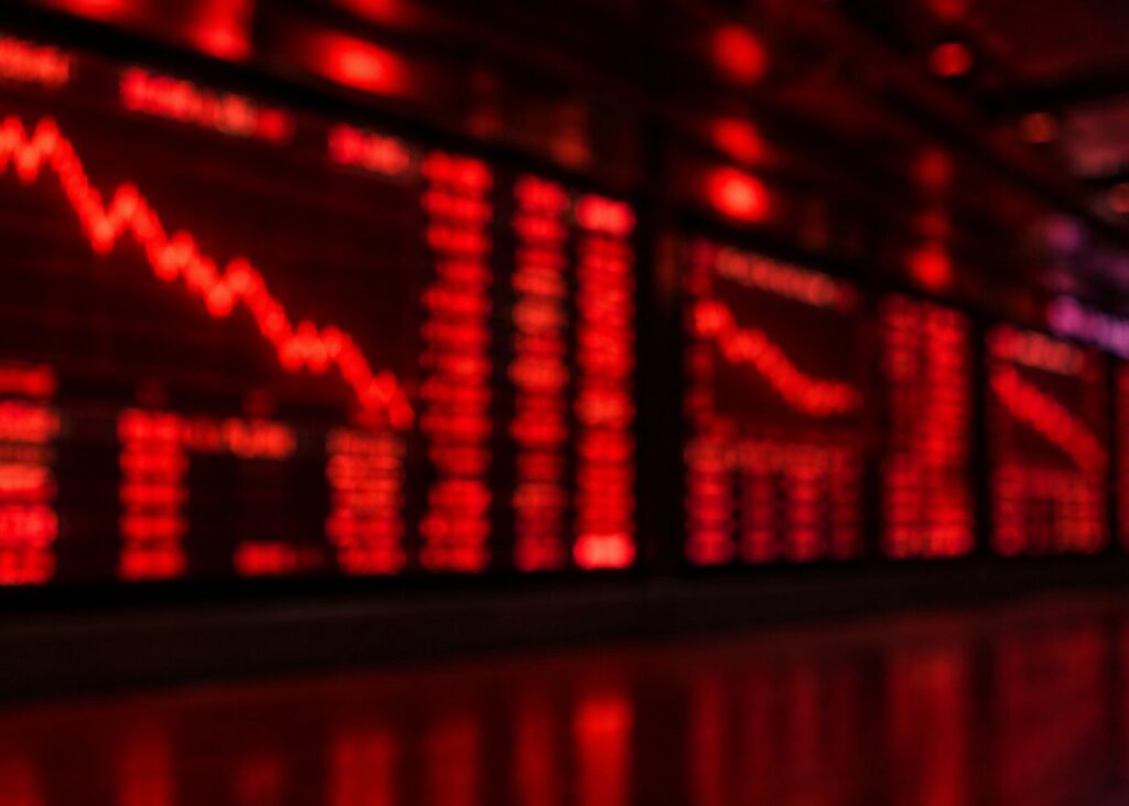 Blurred red stock market trading screens showing falling charts on a dark exchange wall