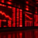 Blurred red stock market trading screens showing falling charts on a dark exchange wall