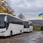 Two coaches parked beside a Ukrainian flag.
